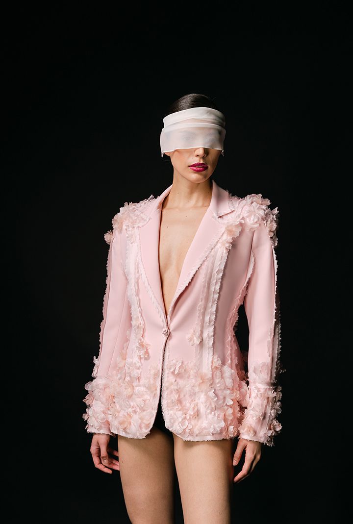 A pink textured blazer styled with light bandage headpiece against black background.