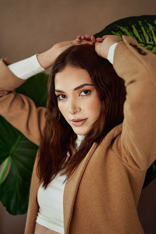 Fashion portrait against tropical leaves backdrop featuring brown jacket and white top.