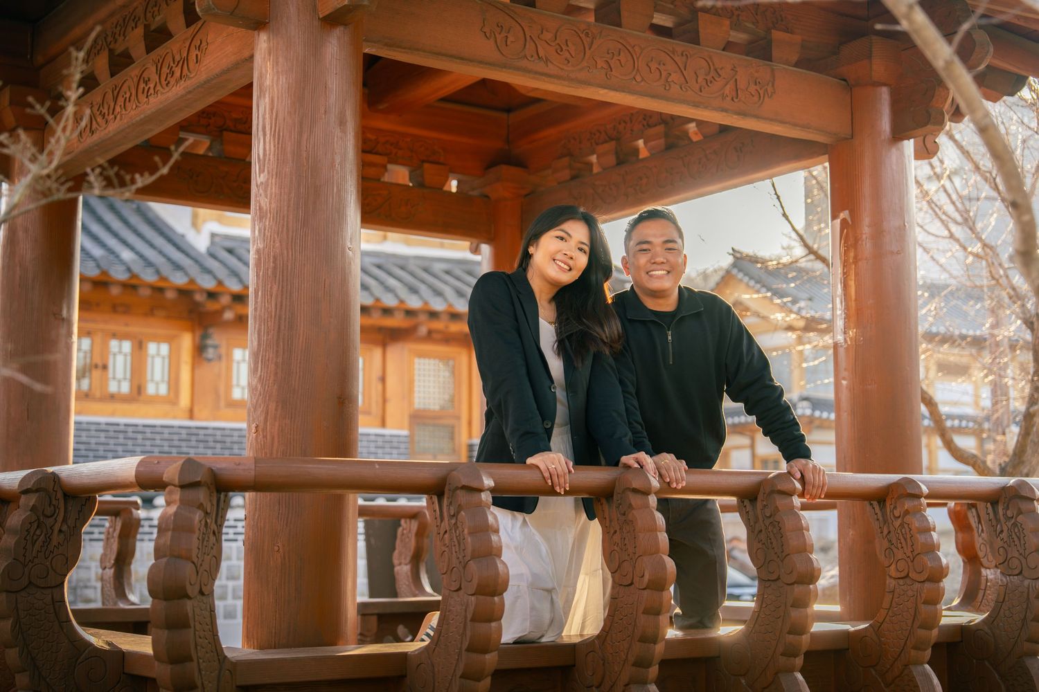 Couple strolling hand in hand through traditional Korean hanok village courtyard with ornate wooden buildings.