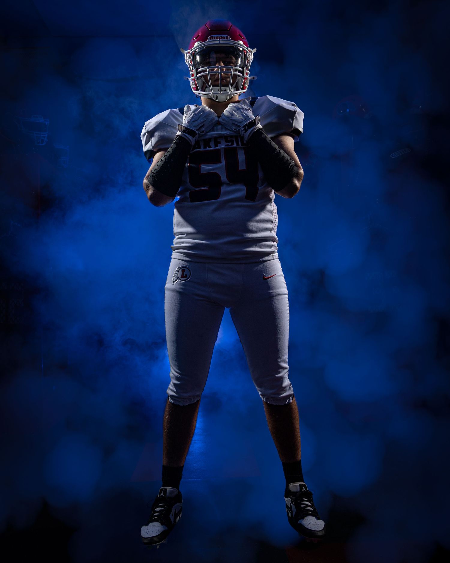 Football player poses in uniform against dramatic blue backdrop, showcasing their athletic stance and protective gear.