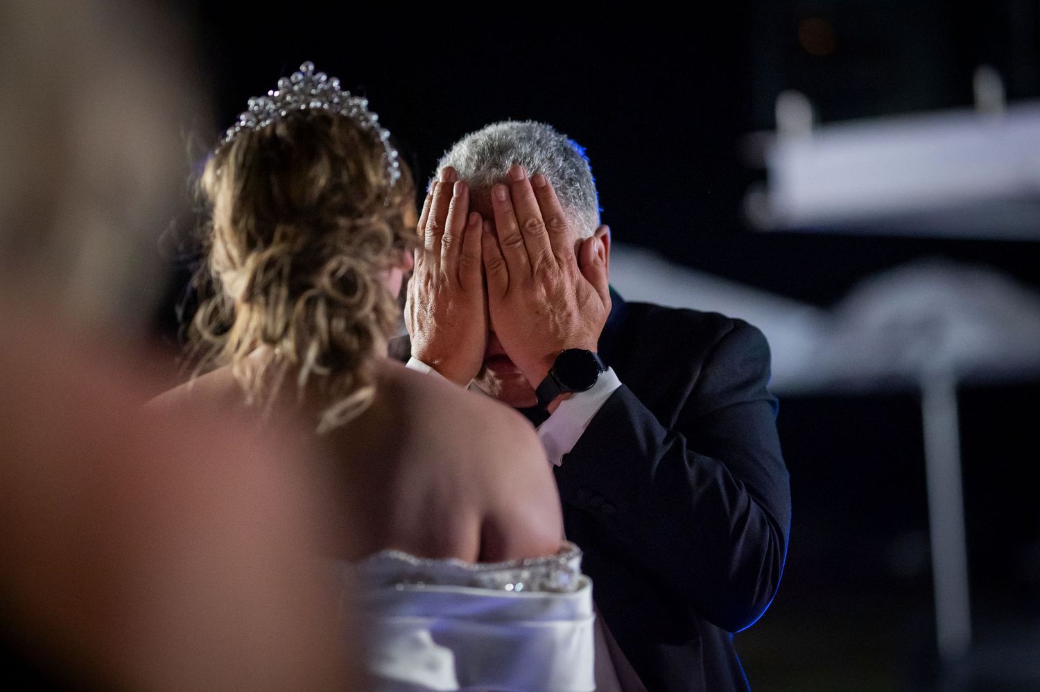 Emotional moment at a wedding reception as someone covers their face while seated next to someone in formal attire.