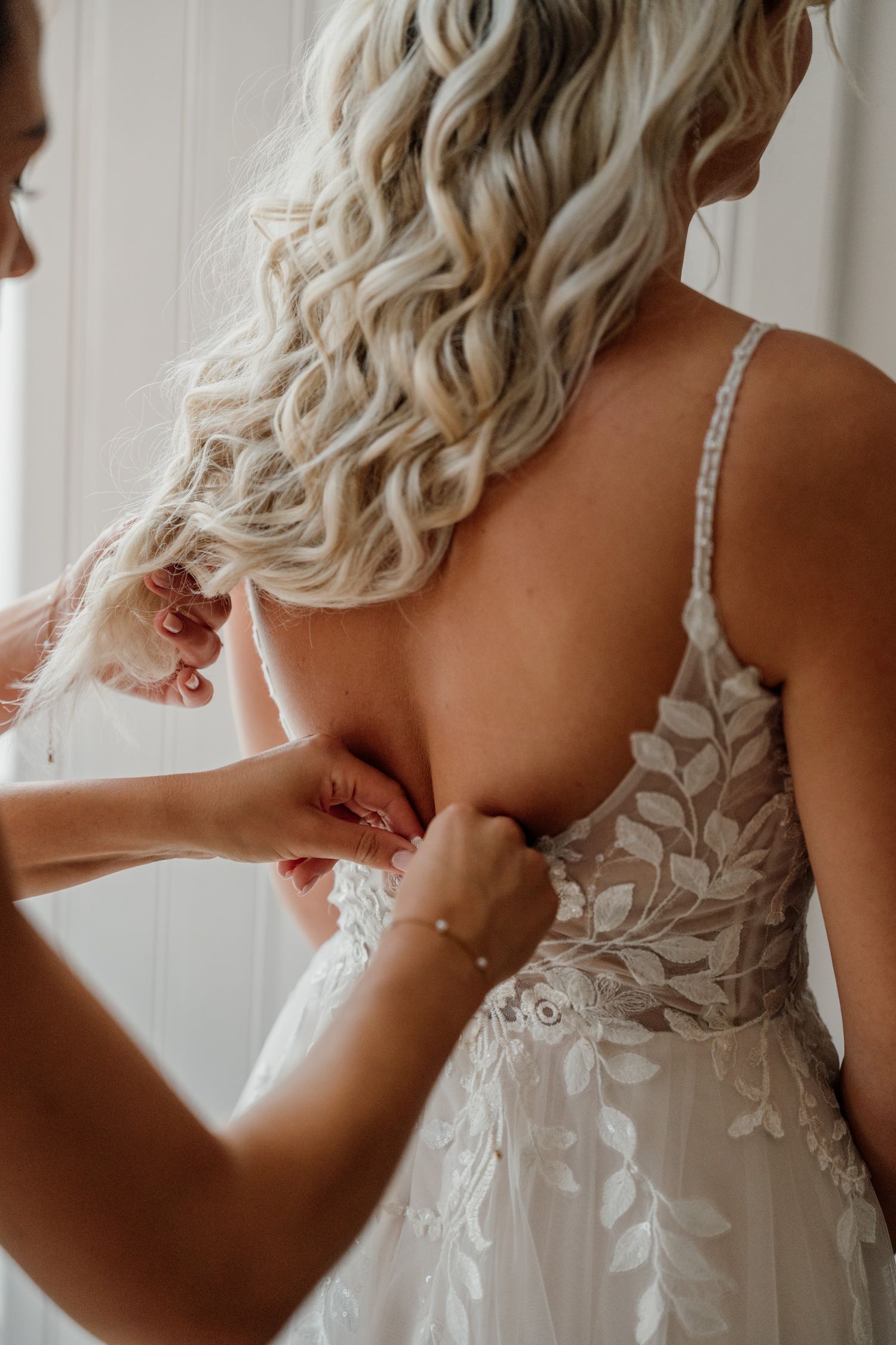 Detail shot of intricate lace wedding dress being buttoned up.
