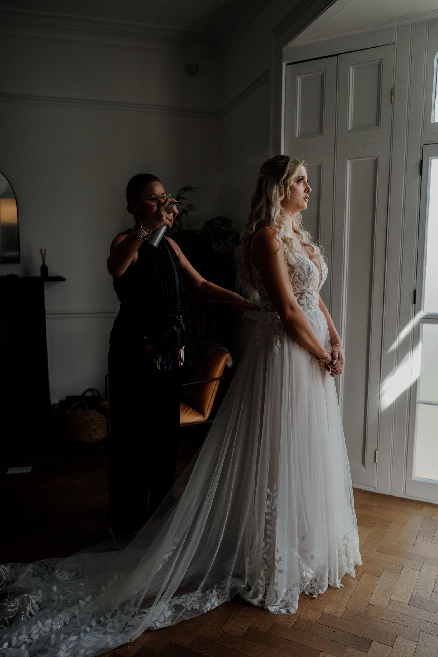 A bride getting ready for her wedding in a naturally lit room with flowing white dress and cathedral veil.