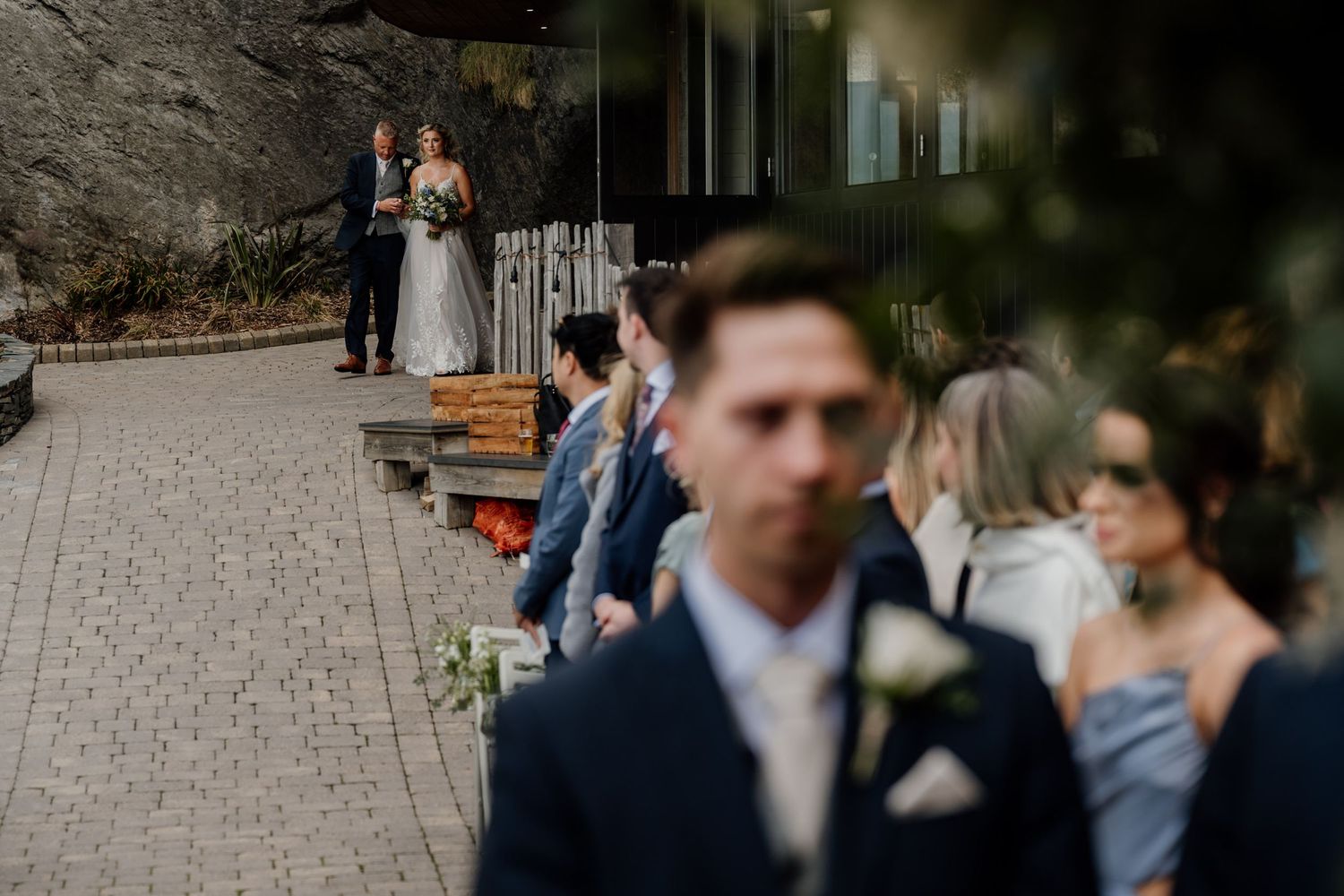 Wedding guests gathering outside a venue with stone walls and modern architecture.