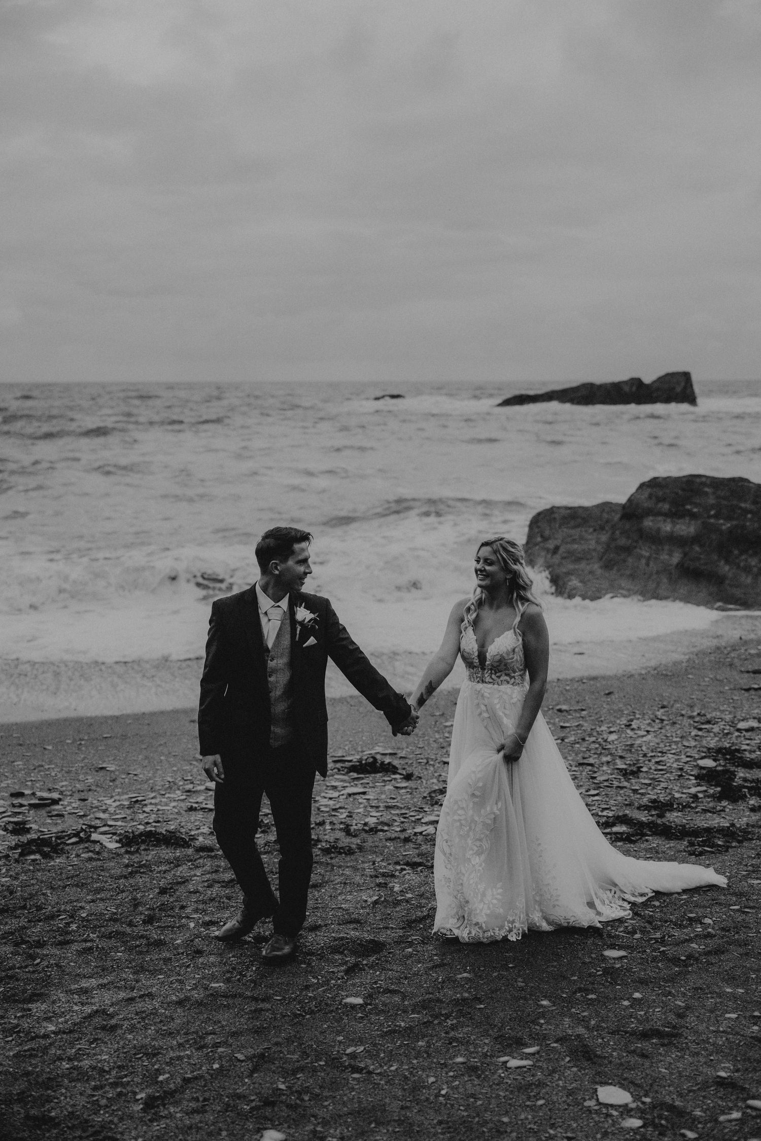 A romantic coastal wedding photoshoot with dramatic ocean views and rocky shoreline in black and white.