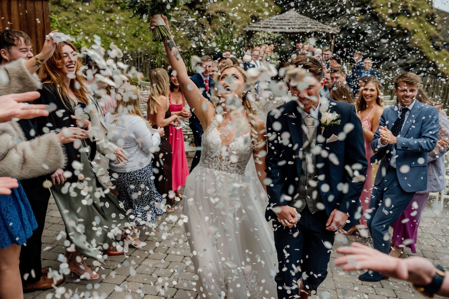 Wedding guests throwing confetti in celebration outdoors on a sunny day.
