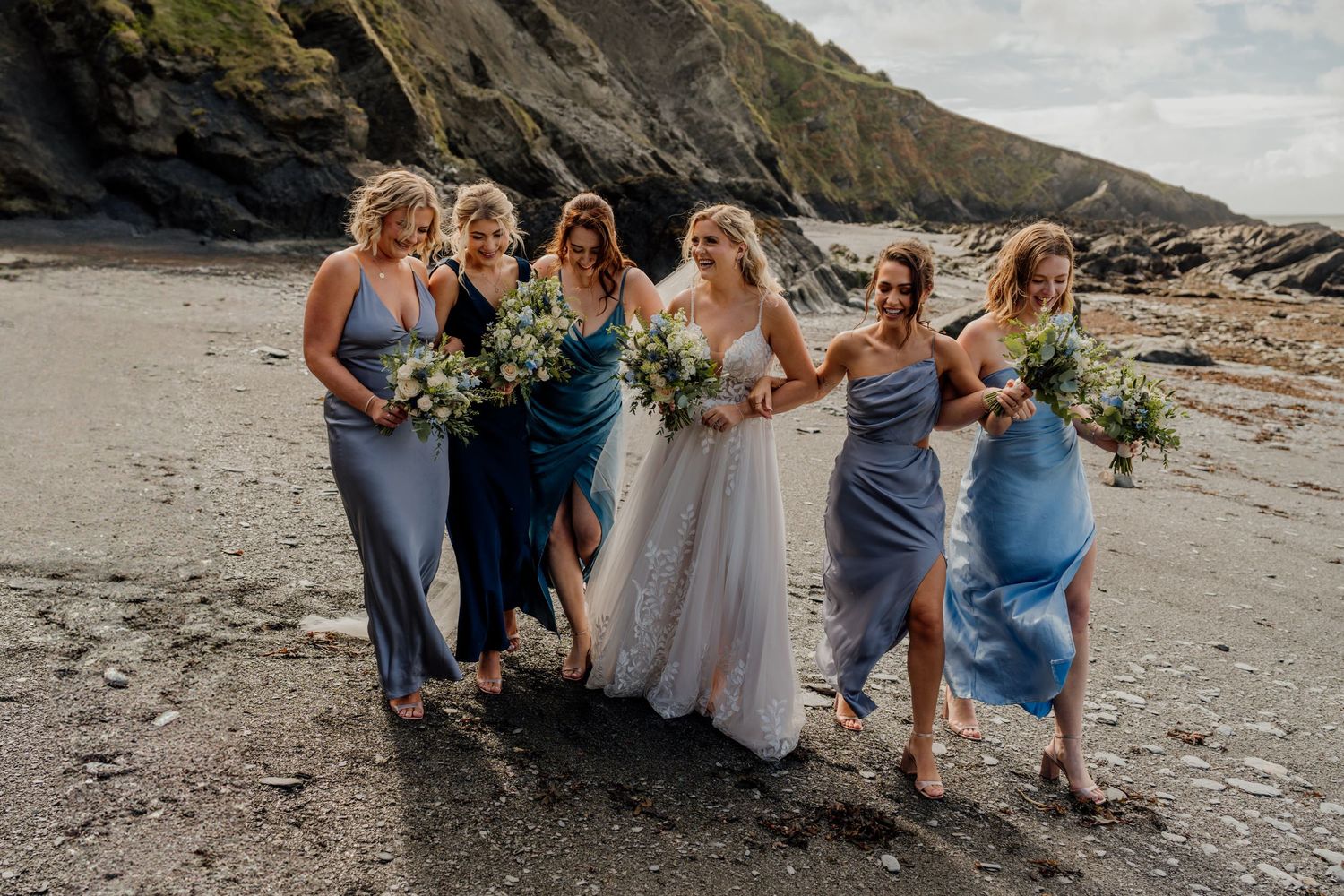 Wedding party gathered on a scenic beach with rugged cliffs in the background.
