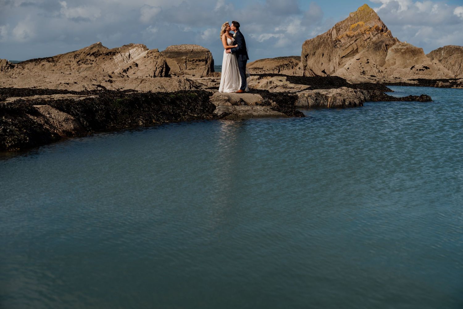 A dramatic coastal wedding photoshoot with rocky cliffs and blue ocean waters in the background.