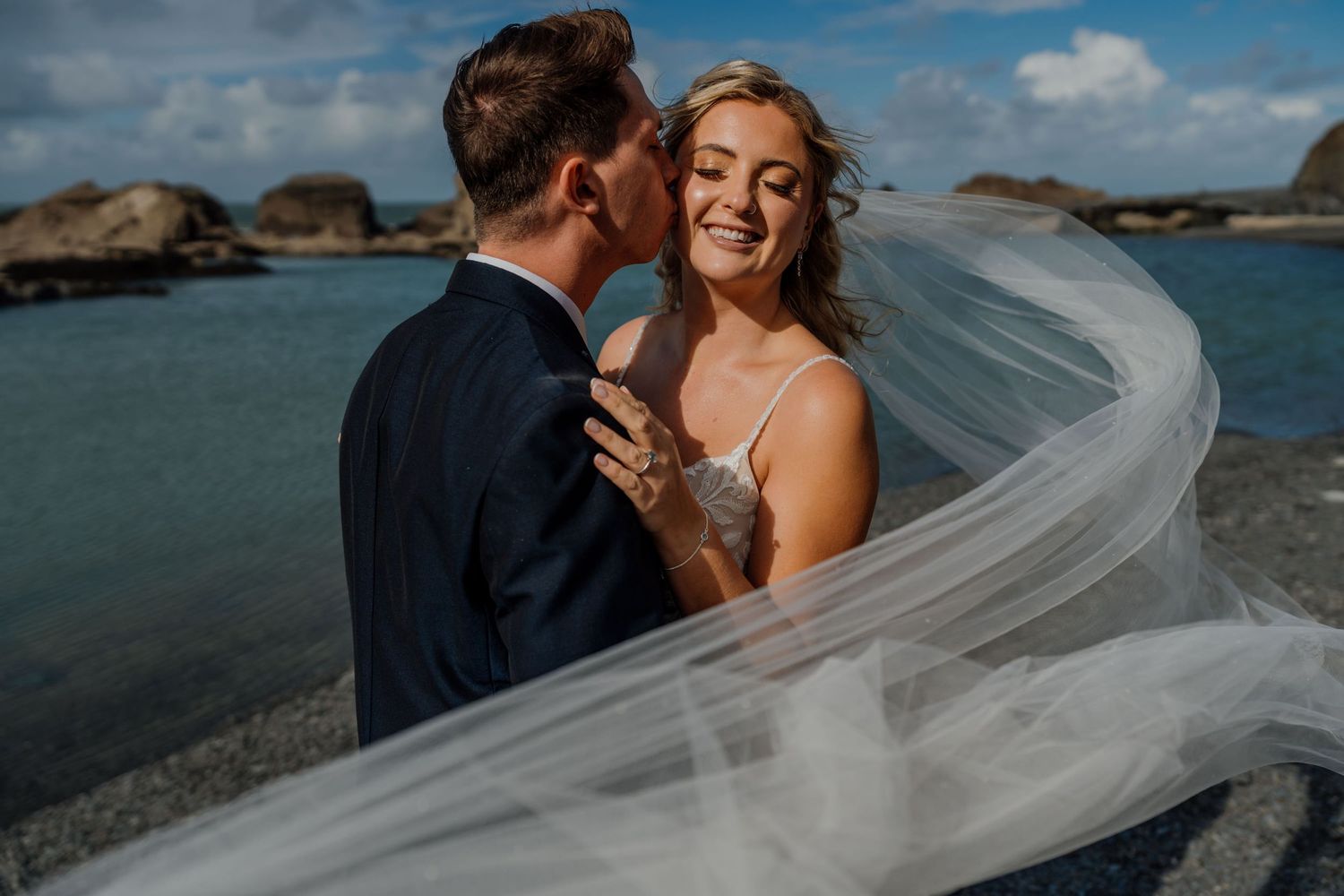 Scenic coastal wedding photoshoot with a flowing white veil catching the ocean breeze.