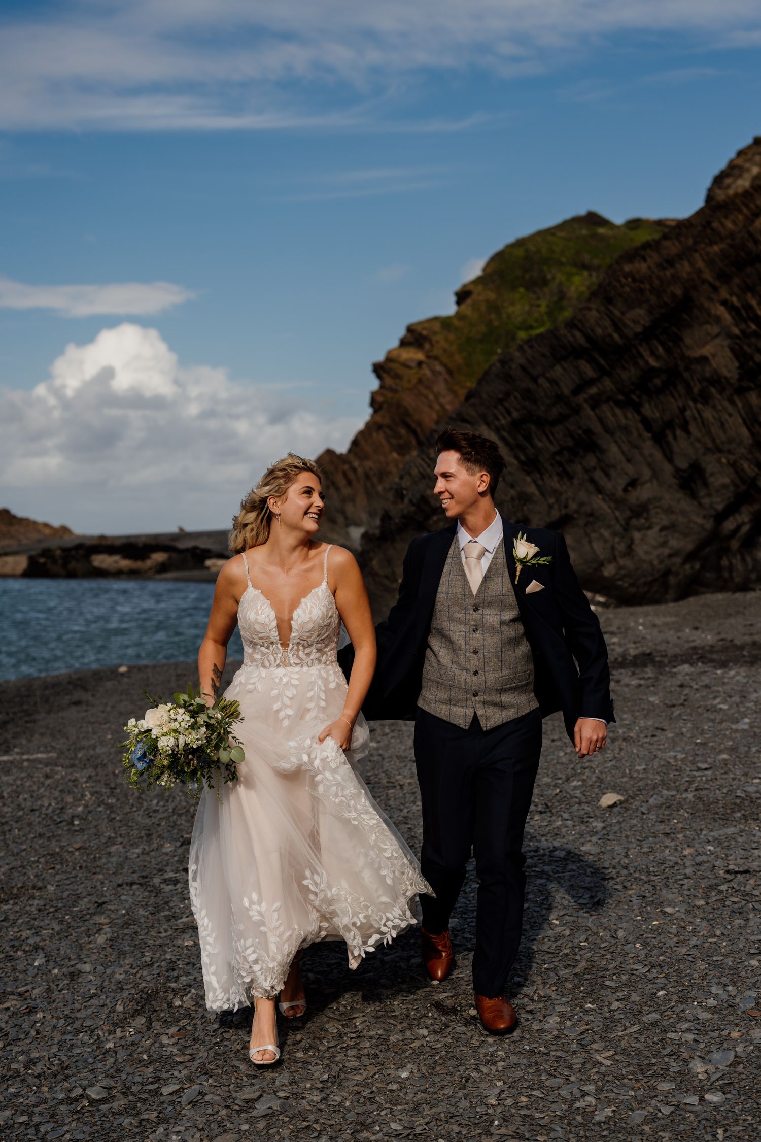 A wedding couple poses together on a dramatic black rocky beach with cliffs and ocean in the background.