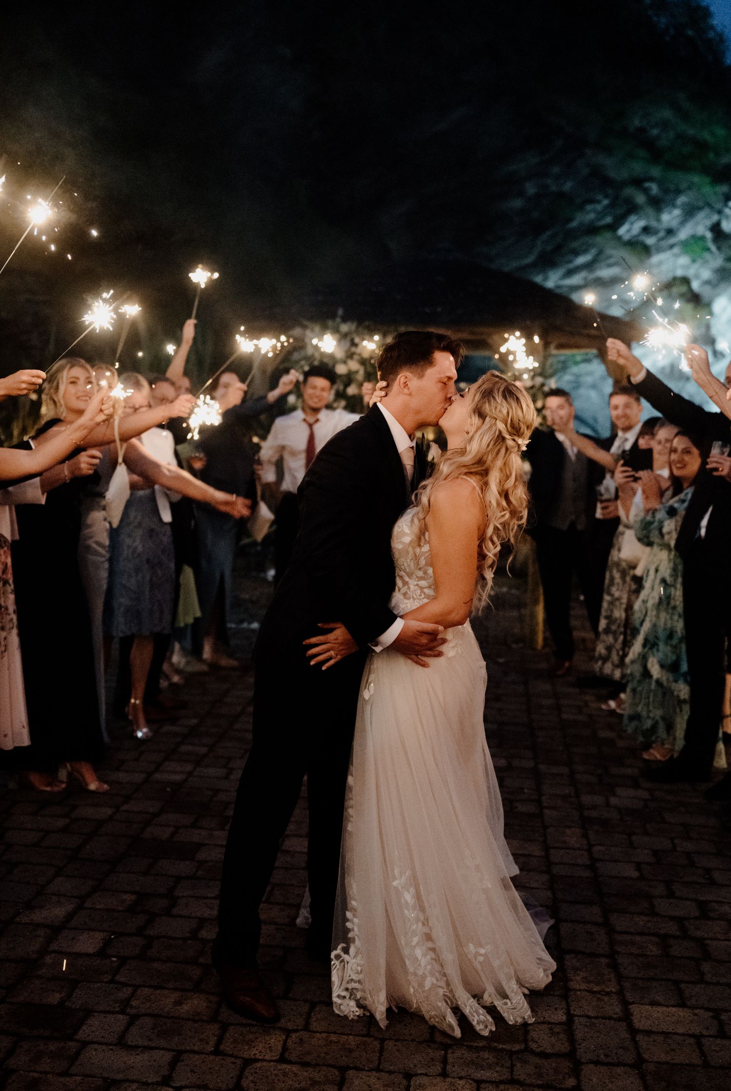Nighttime celebration with sparklers surrounding a couple during their first dance on a brick patio.
