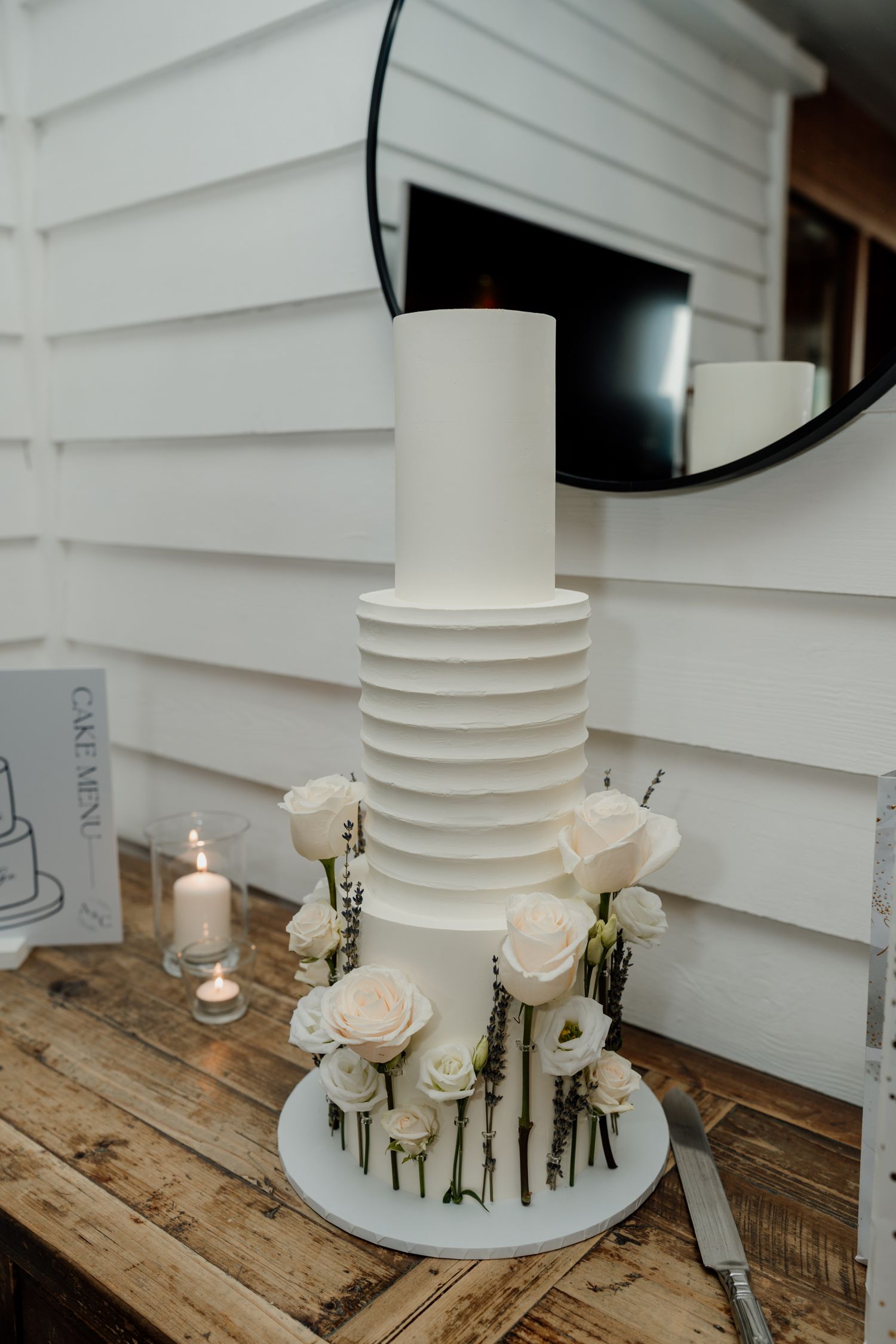 Elegant white wedding cake with fresh floral decorations displayed on a rustic wooden table.