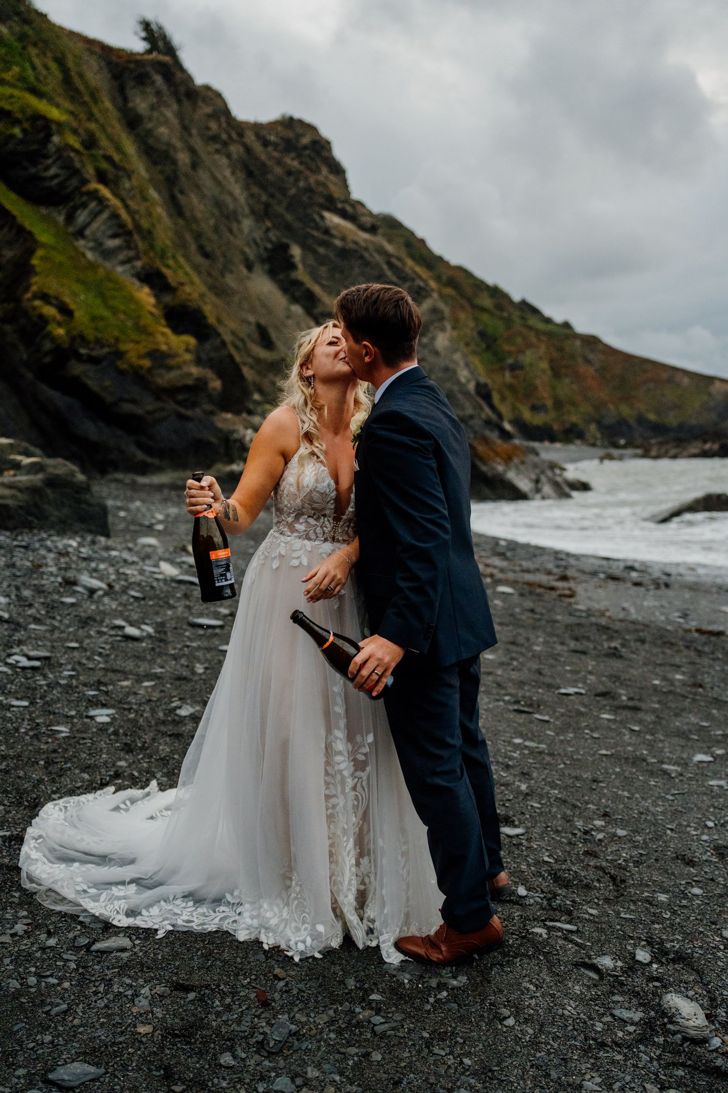 Wedding couple celebrating with champagne on a dramatic black sand beach with cliffs in the background.