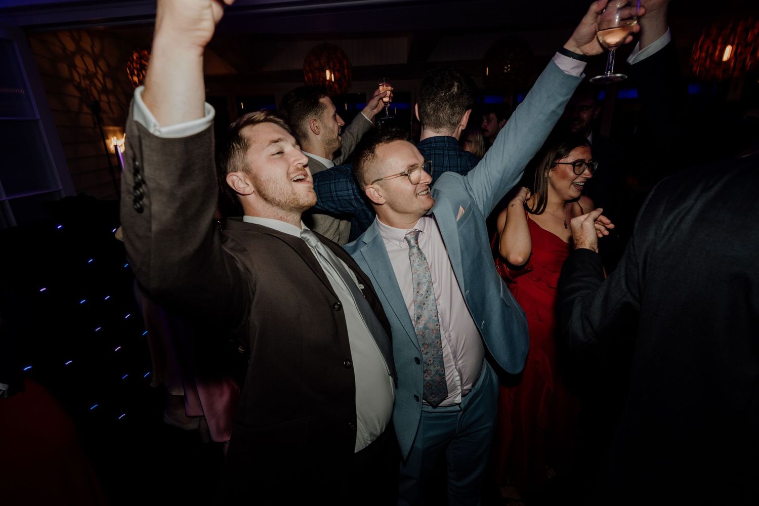 Wedding guests dancing and celebrating at a darkened reception venue.