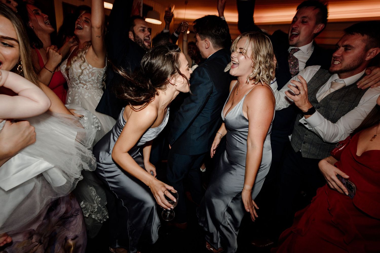 Wedding reception guests dancing and celebrating in a dimly lit venue with red ambient lighting.