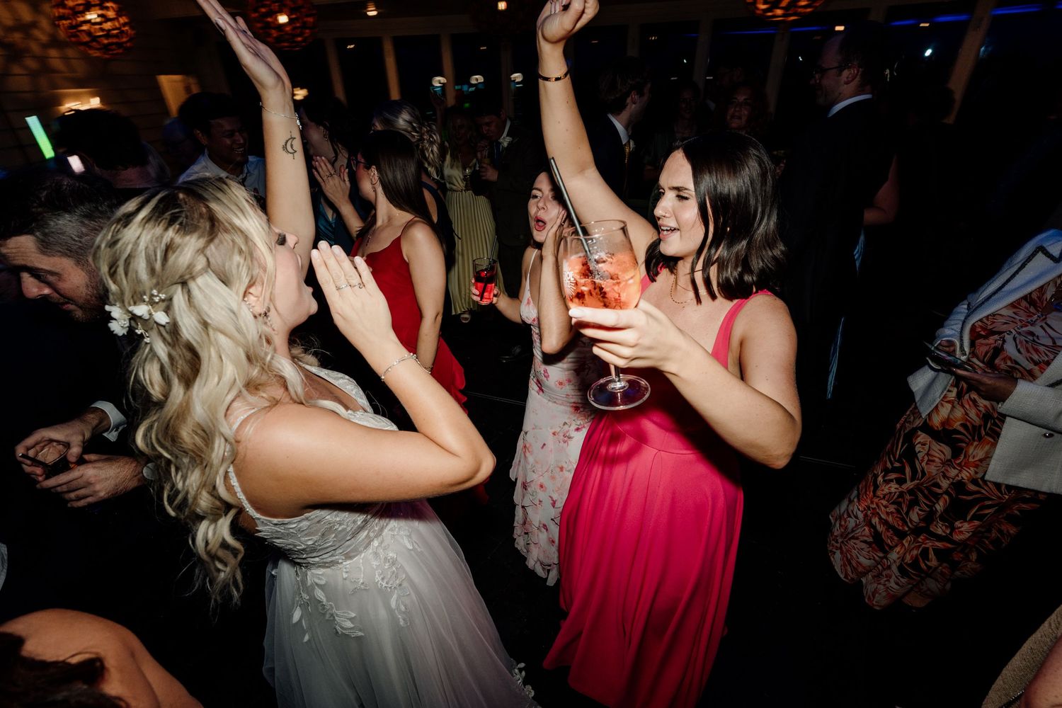 Party guests dancing and celebrating at a wedding reception in dark atmospheric lighting.