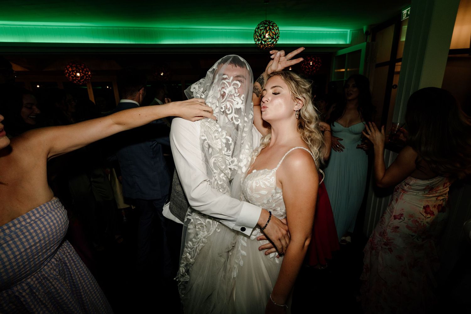 Lively dance floor scene with green lighting at a wedding reception celebration.