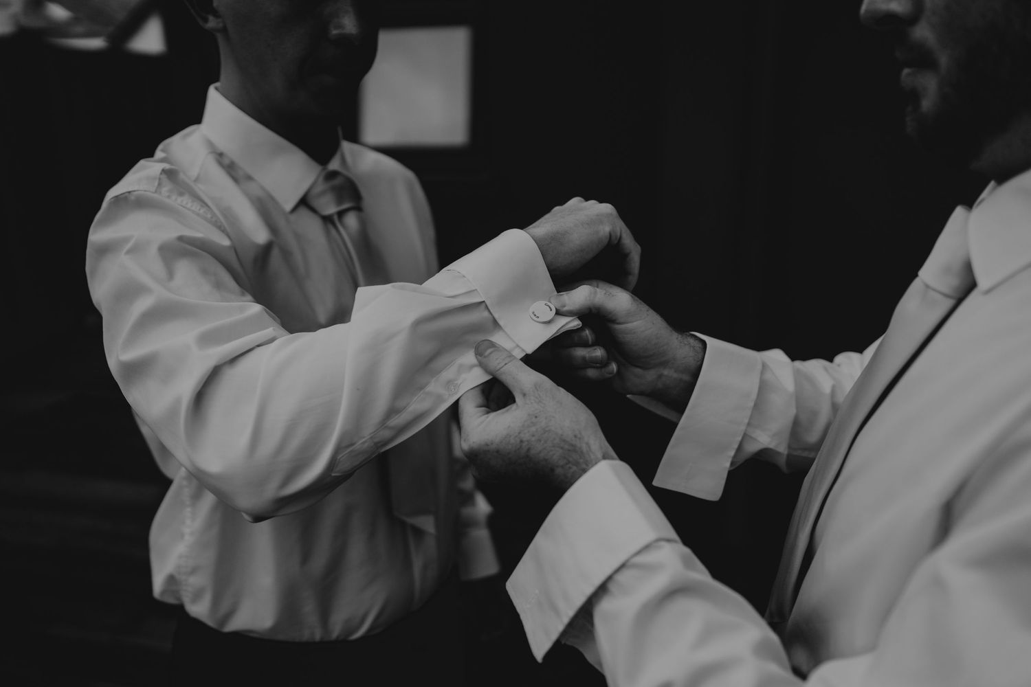 Black and white image of people adjusting formal attire before an event.