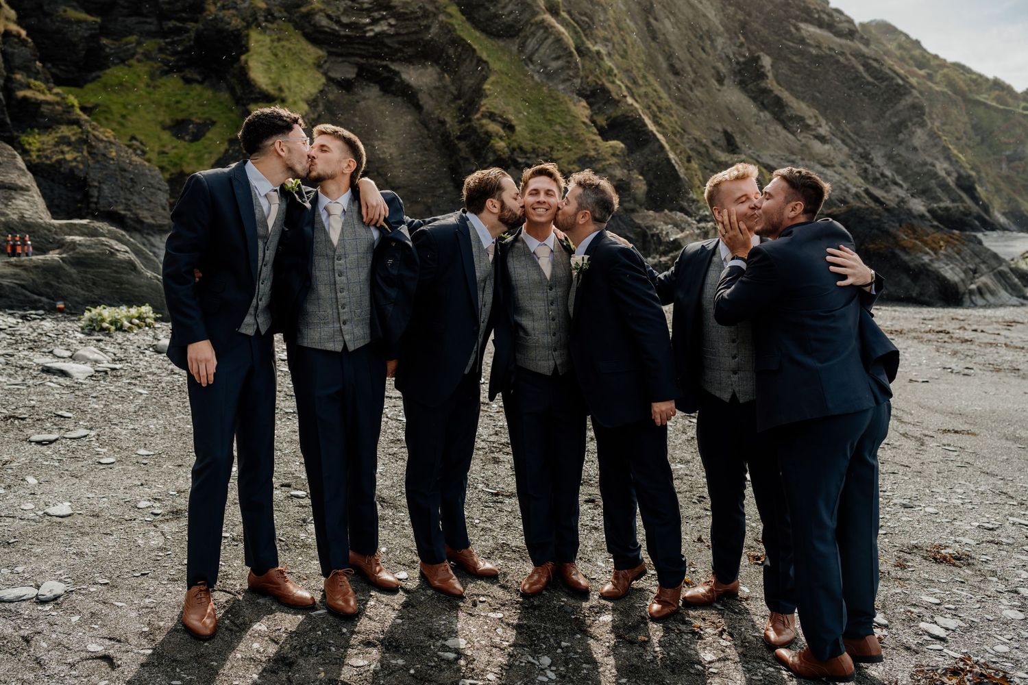 Wedding party posing together on rocky beach coastline in formal attire.