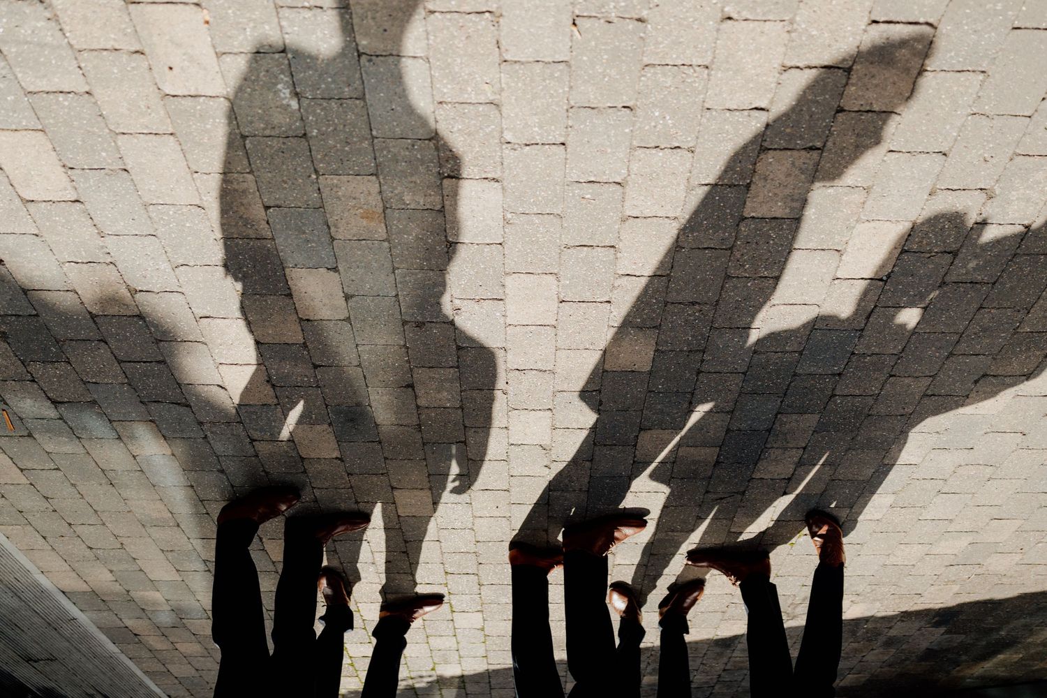 Shadow silhouettes of a wedding party cast dramatically against a white brick wall.