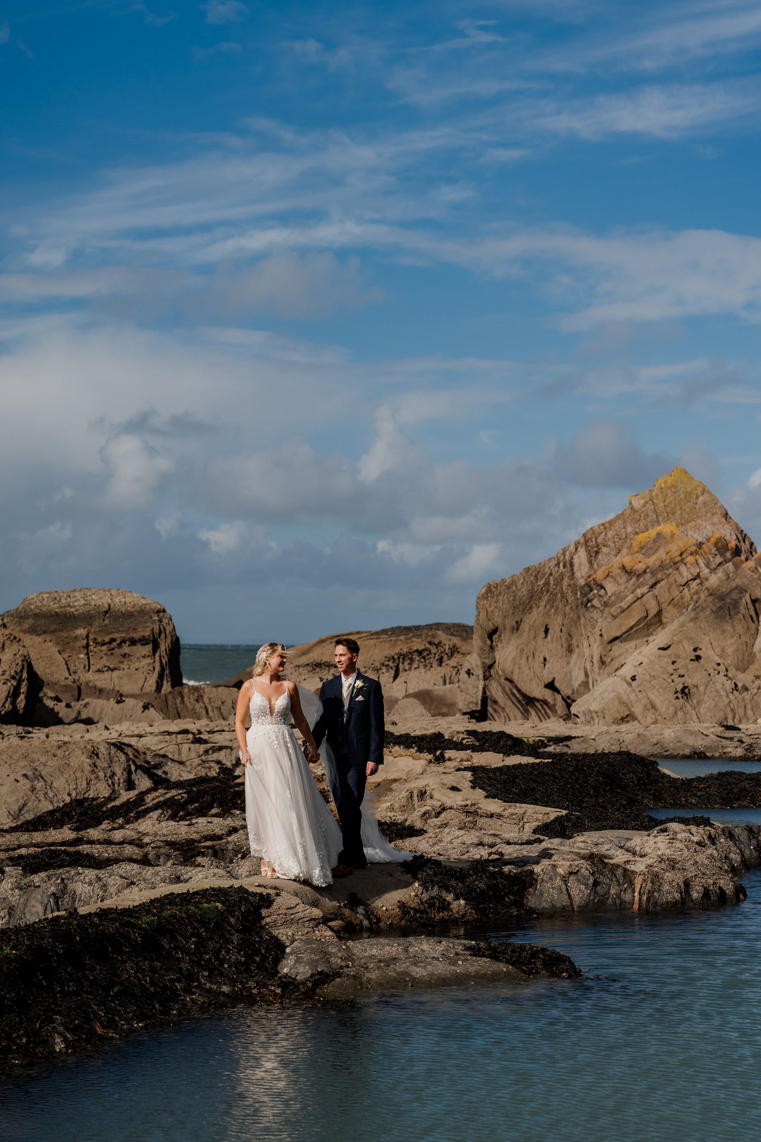 Scenic coastal wedding photography with dramatic rocky cliffs and blue ocean backdrop.