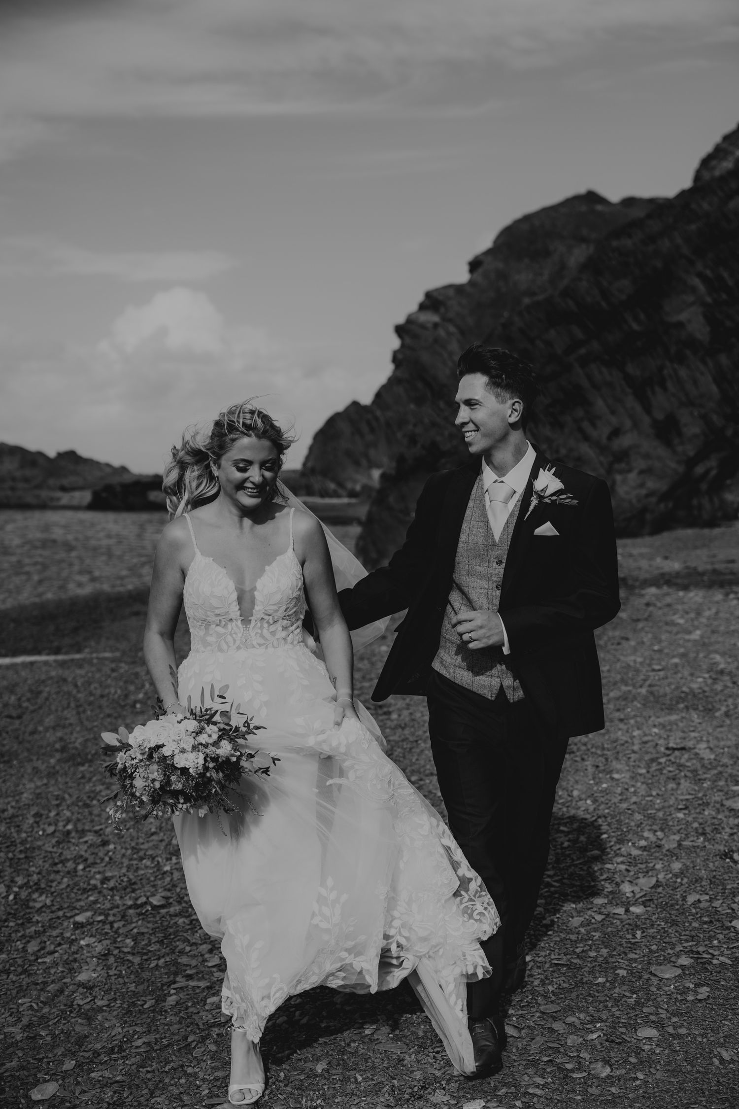 Black and white wedding portraits on a dramatic coastal landscape with rocky cliffs.