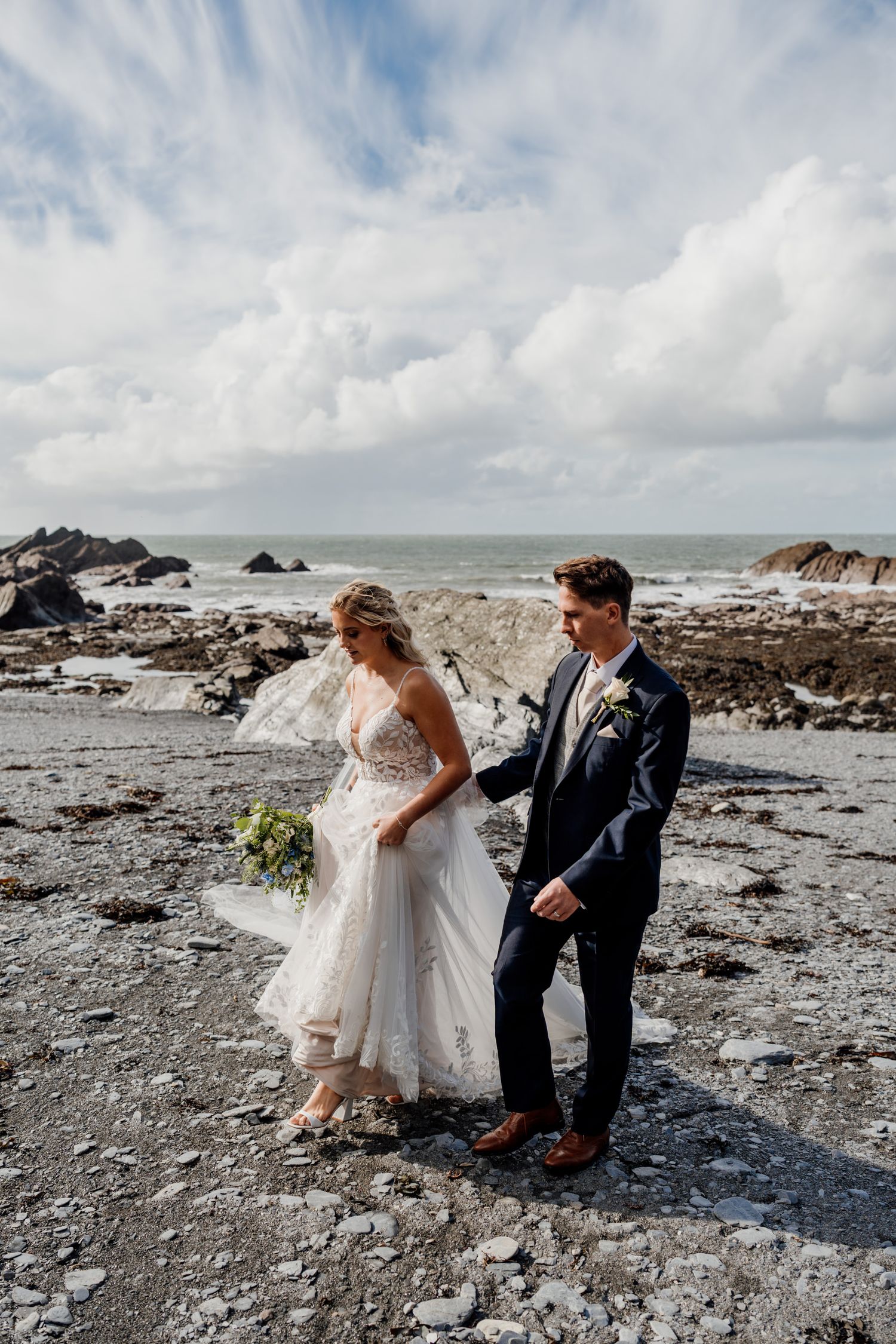 A romantic beach wedding photoshoot with dramatic coastal cliffs and crashing waves in the background.