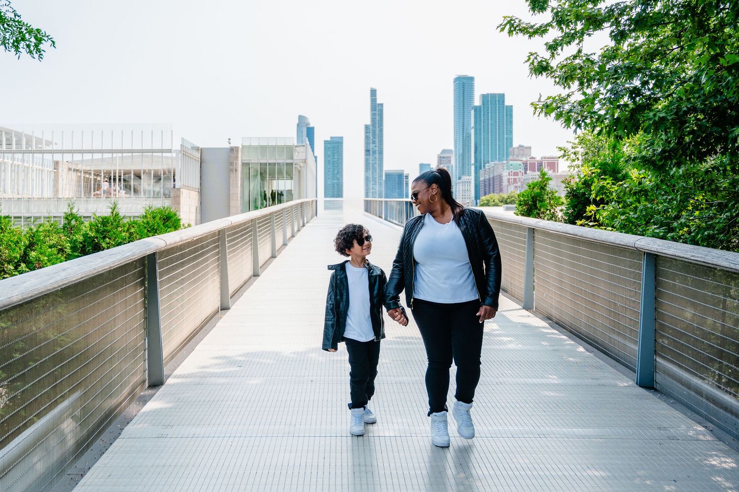 A family walk along an elevated concrete pathway with city skyline and greenery in the background.