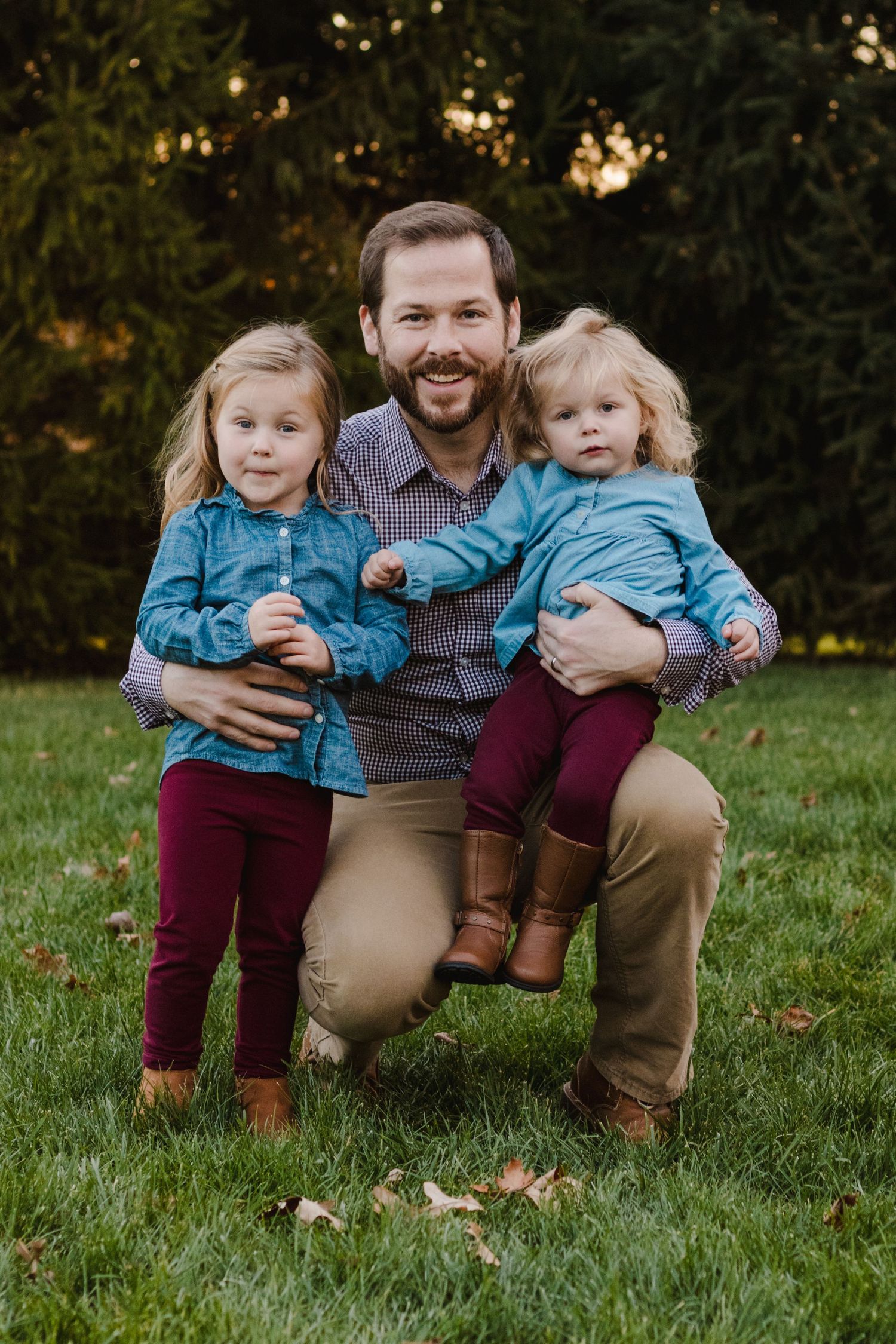 Father keeling with his two daughters smiling during a lifestyle family photography golden hour session in South Lyon, Michigan.