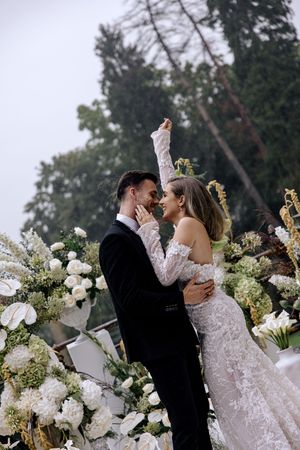 Newlyweds share tender kisses in a romantic setting filled with white hydrangeas and floral arrangements.