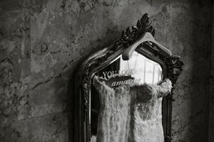 An ornate antique mirror with an elaborate black frame hangs against a weathered concrete wall.