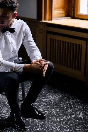 Person in white dress shirt sitting on patterned carpet in dramatic window lighting.