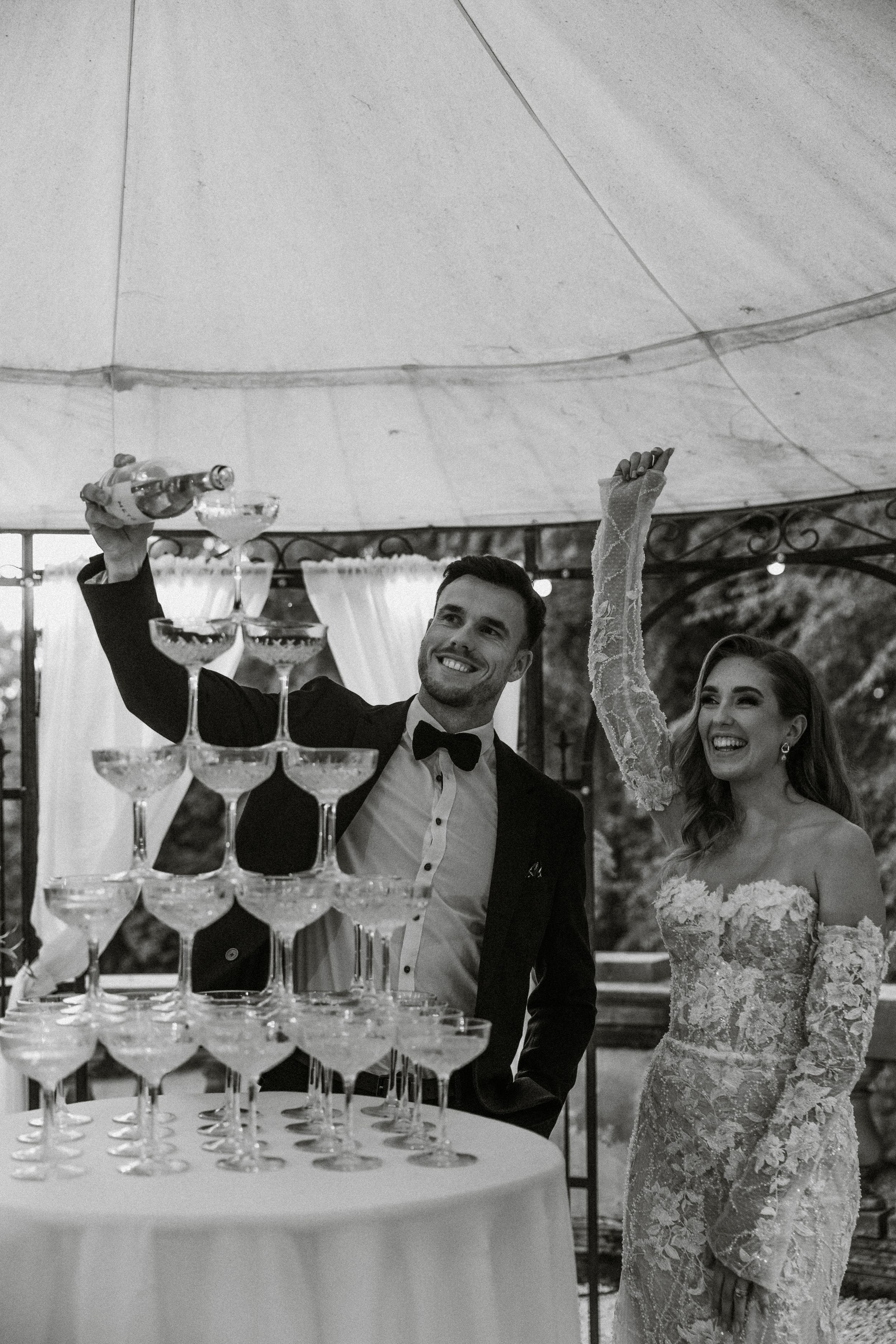 Newlyweds celebrate with champagne tower pour at elegant tented wedding reception.