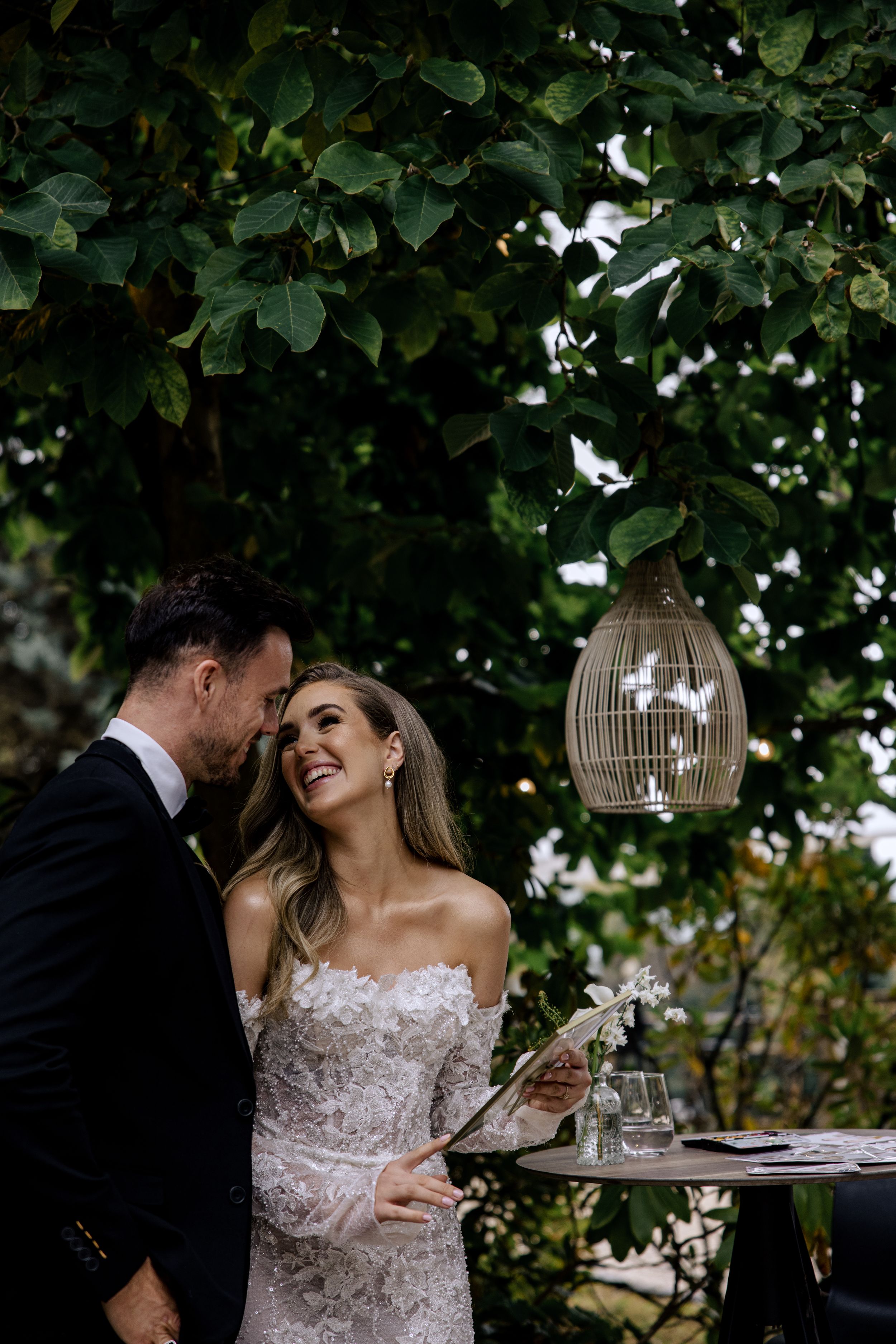 Wedding couple shares intimate moments surrounded by lush garden greenery and decorative birdcages during outdoor celebration.