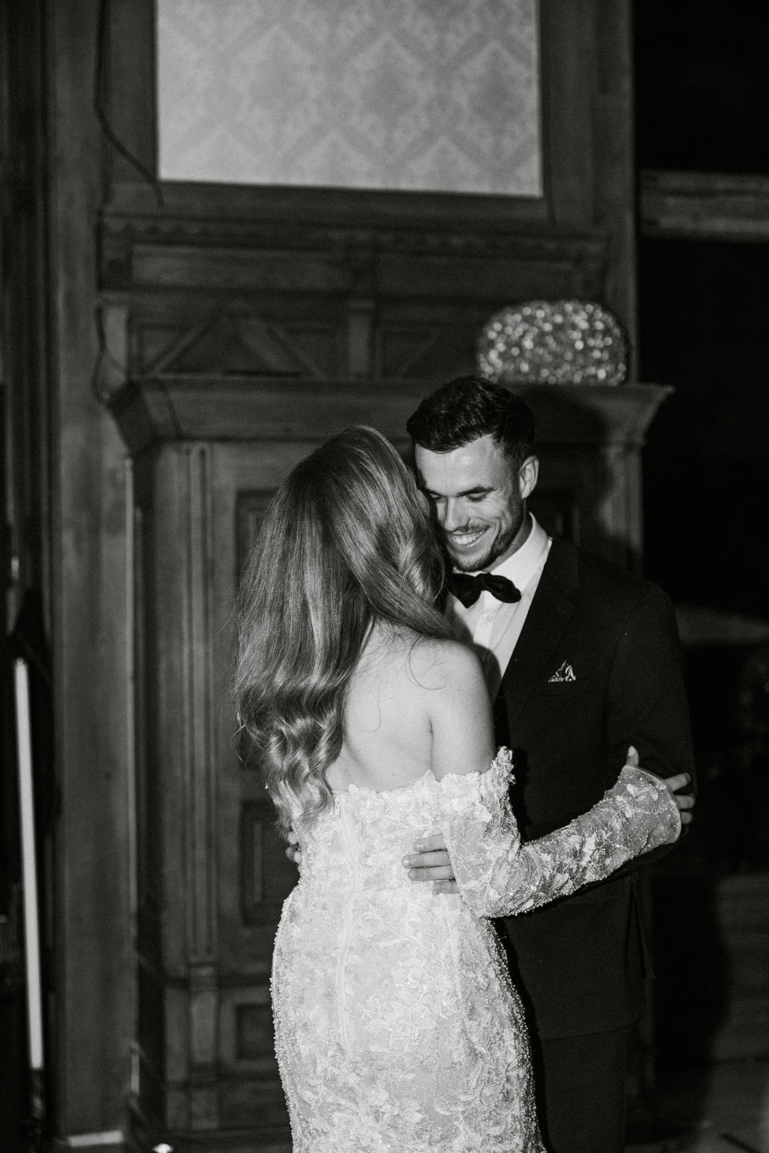 A romantic black and white wedding photo of a couple sharing an intimate moment in formal attire.
