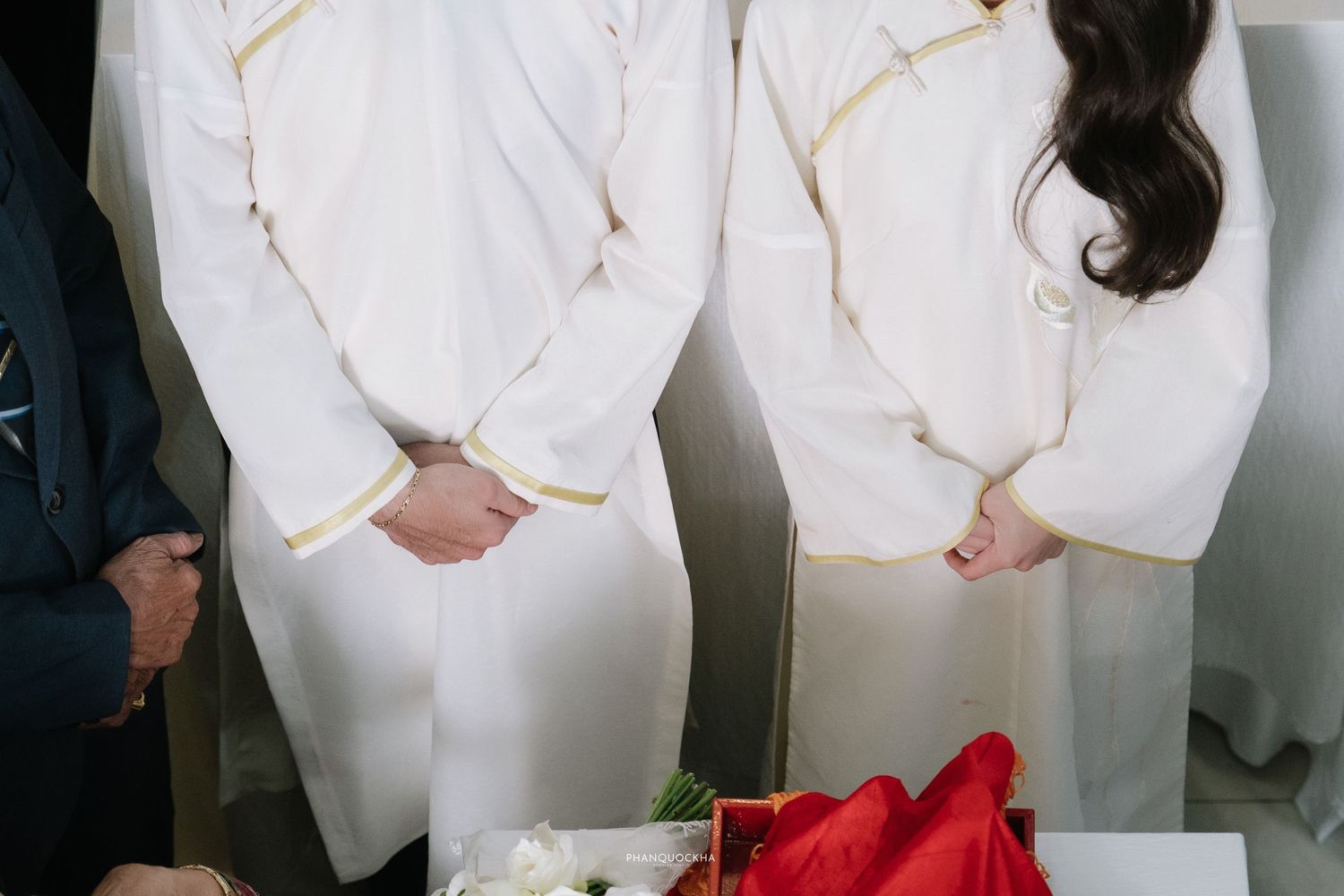 Couple in matching white and gold trimmed traditional Vietnamese ao dai standing at a ceremony.
