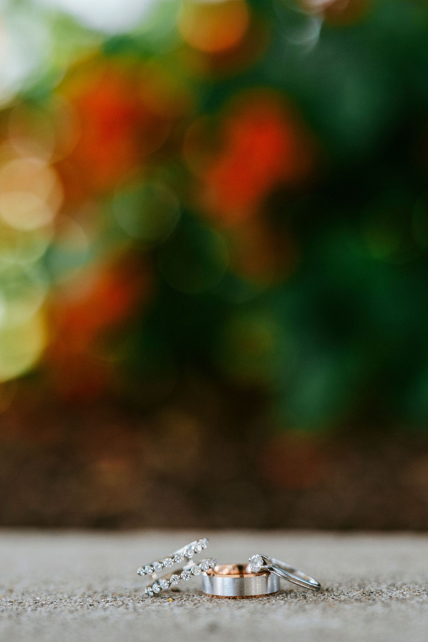 Wedding rings with diamonds sit on a textured gray surface with a blurred orange and green bokeh background.