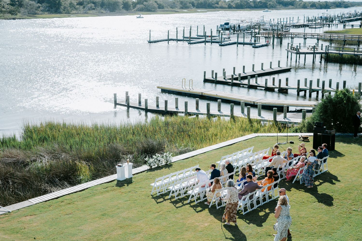 Wedding guests seated on white chairs overlooking a scenic marina with multiple boat docks extending into the water.