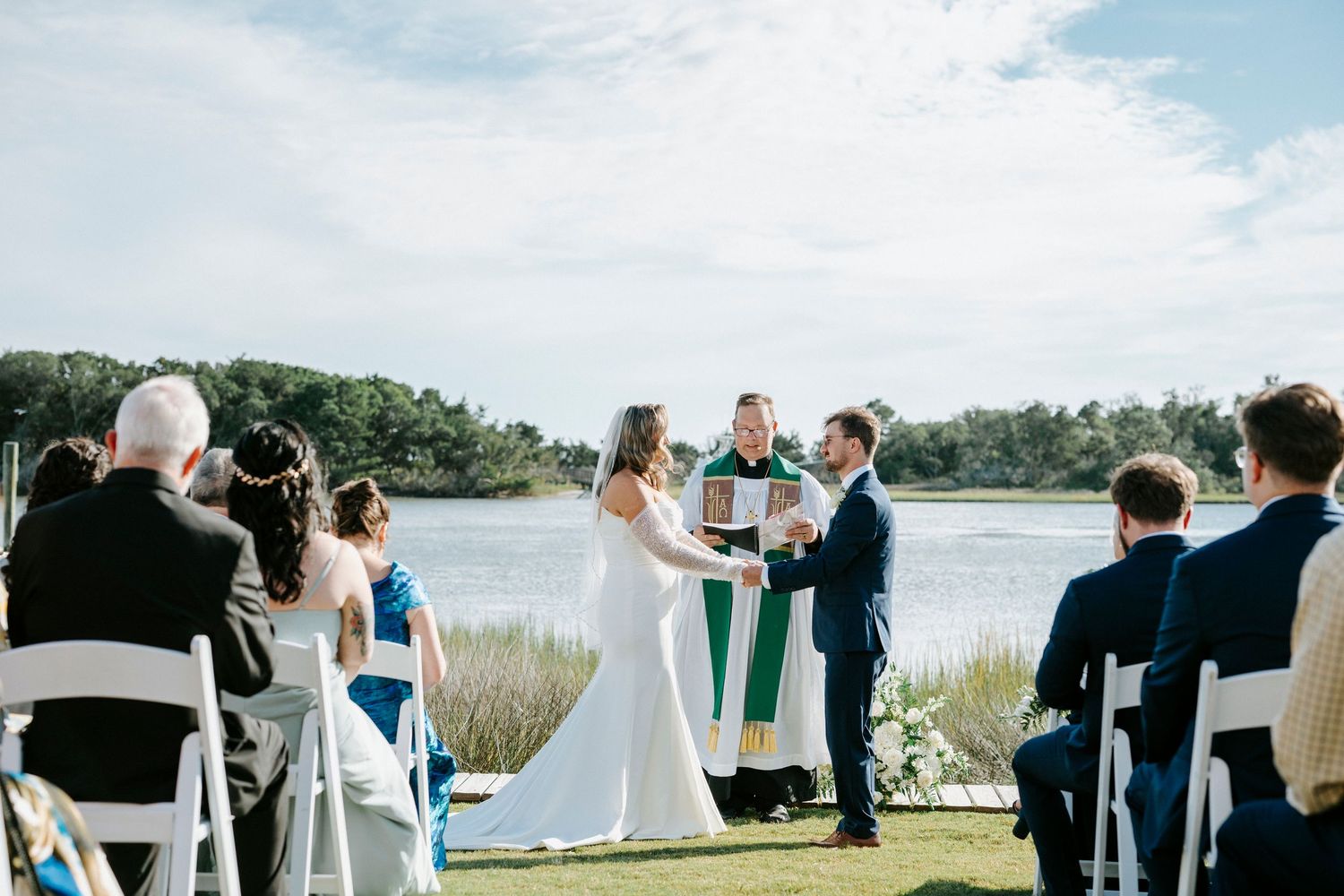 Waterfront outdoor wedding ceremony setup with chairs facing the scenic bay and grassy lawn.