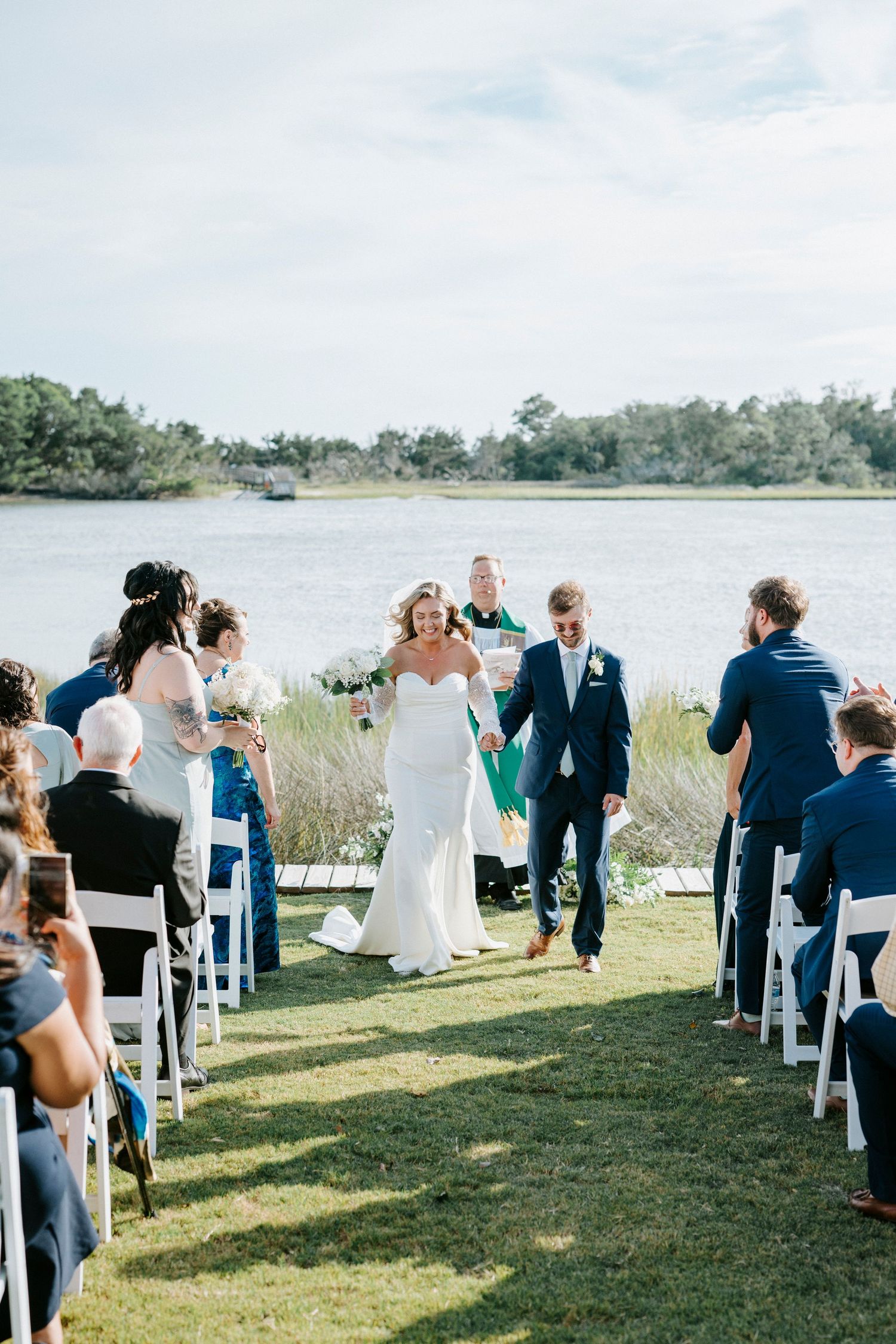 Wedding guests seated on white chairs for outdoor waterfront ceremony overlooking the bay.