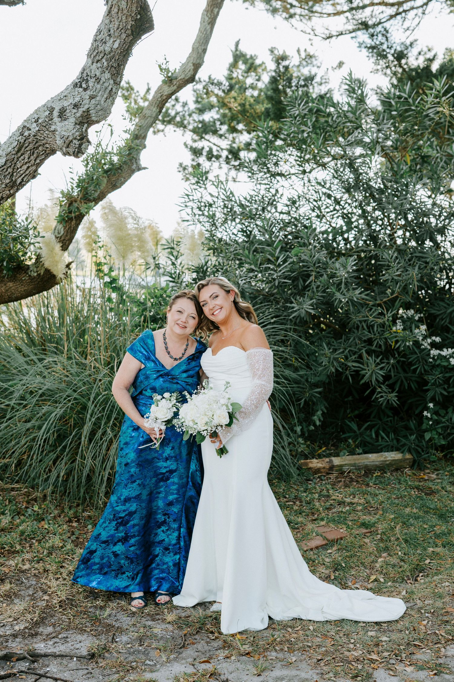 Two people share a joyful moment outdoors with windswept grasses and trees creating a natural backdrop.