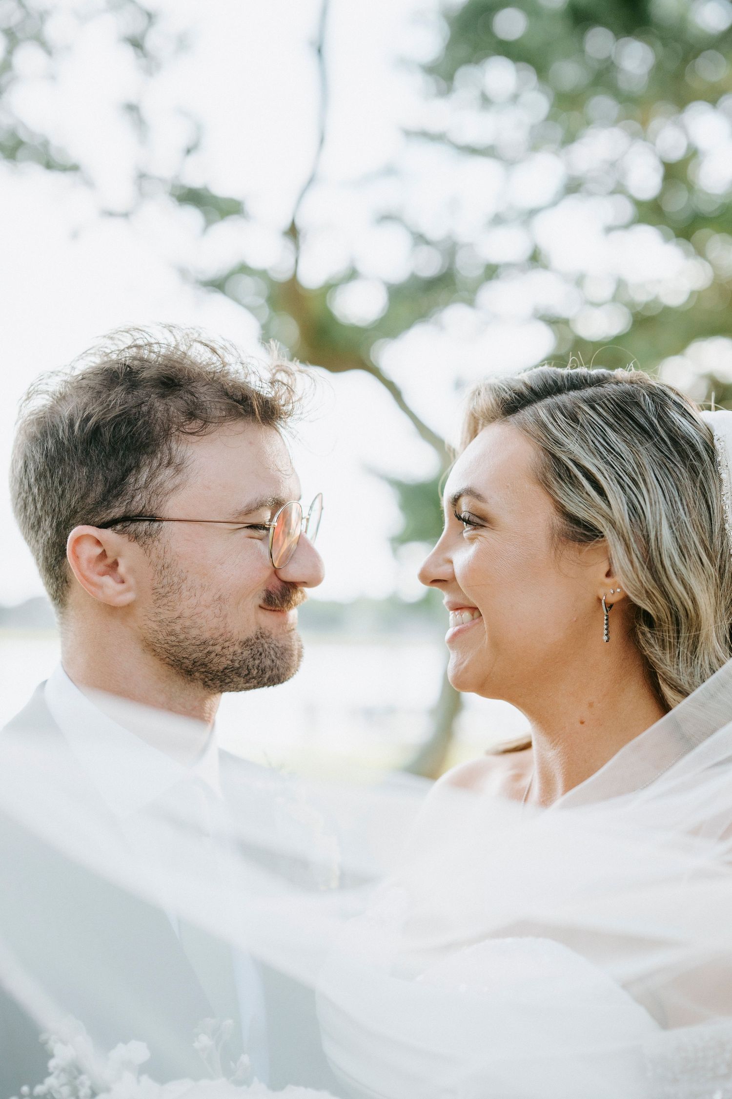 Close-up portrait of a joyful wedding couple through sheer white veil fabric.