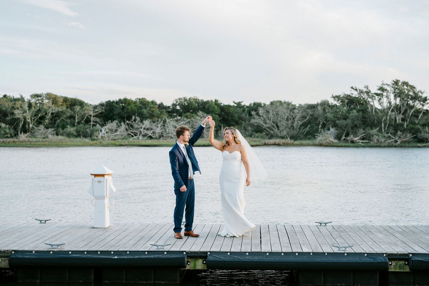 Wedding couple and wedding party pose on a wooden dock by a serene waterfront.