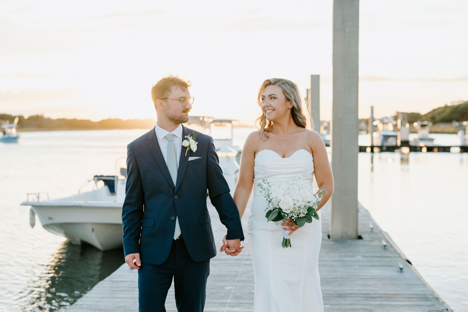 Romantic waterfront wedding photos at sunset with marina and boats in background.