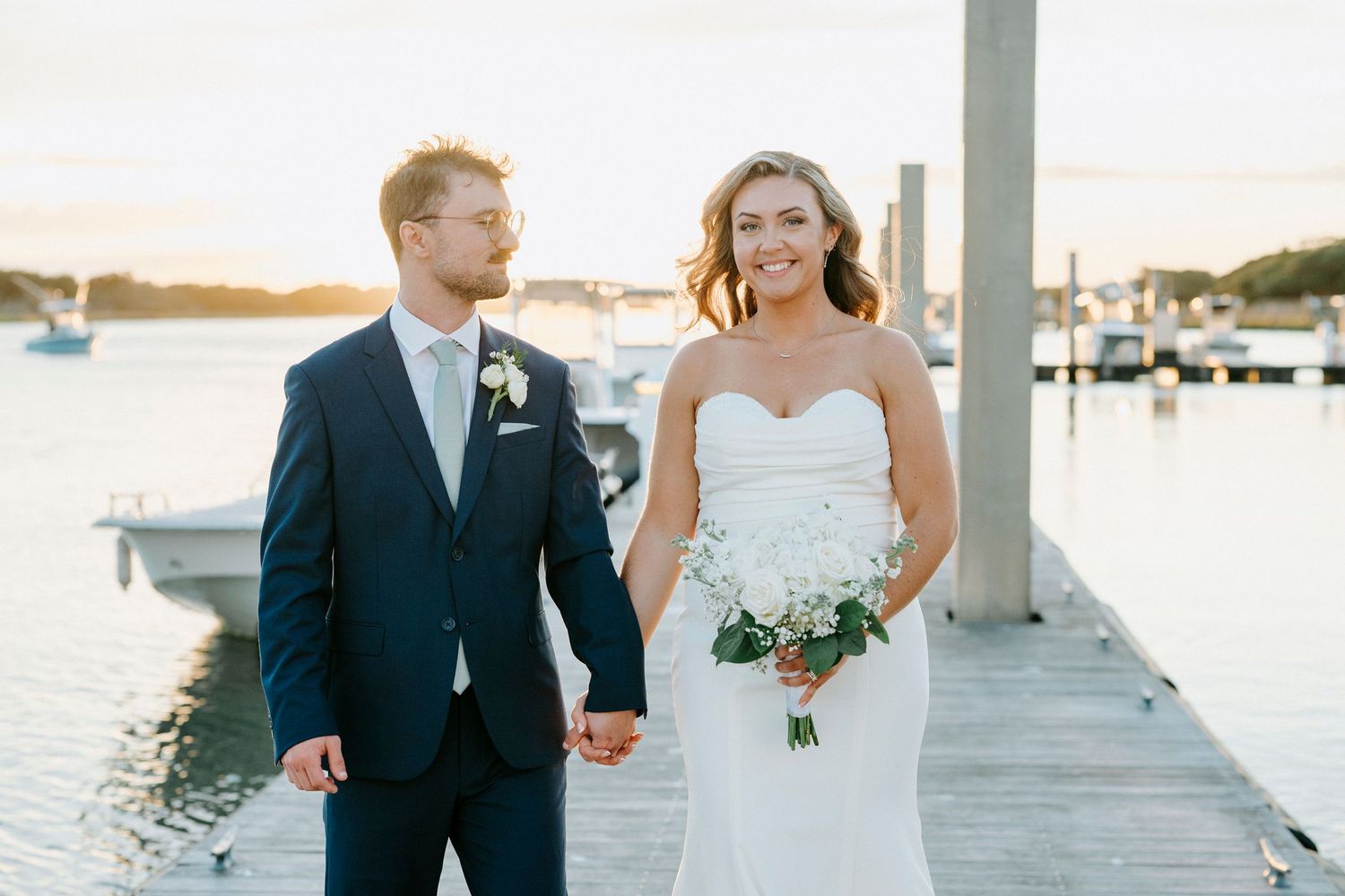 Newlyweds walking along marina dock during golden hour sunset photography session.