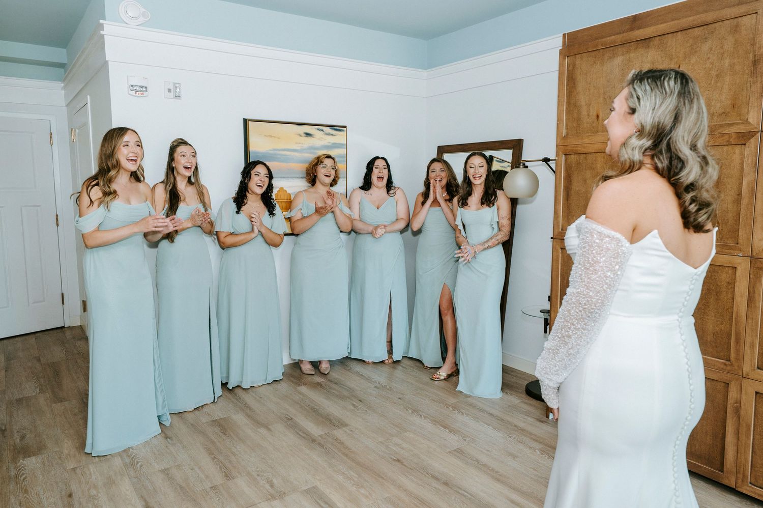 Wedding party in light blue dresses lined up against white wall for group photo.
