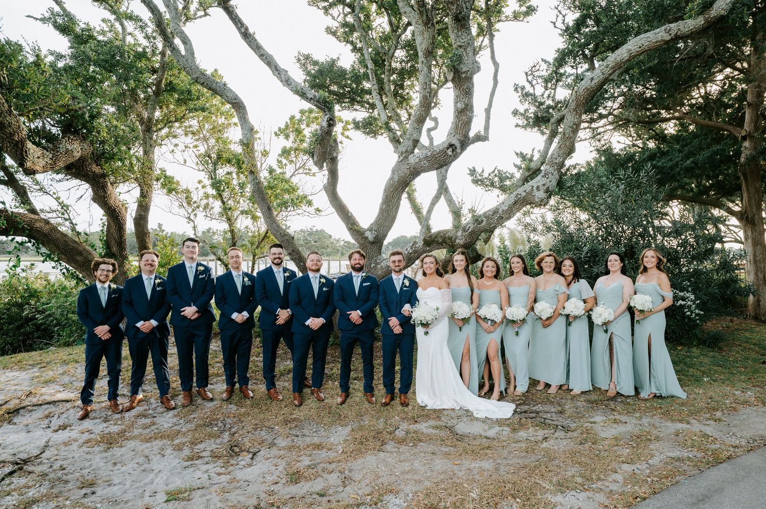 Wedding party poses under majestic oak trees in a natural outdoor setting.