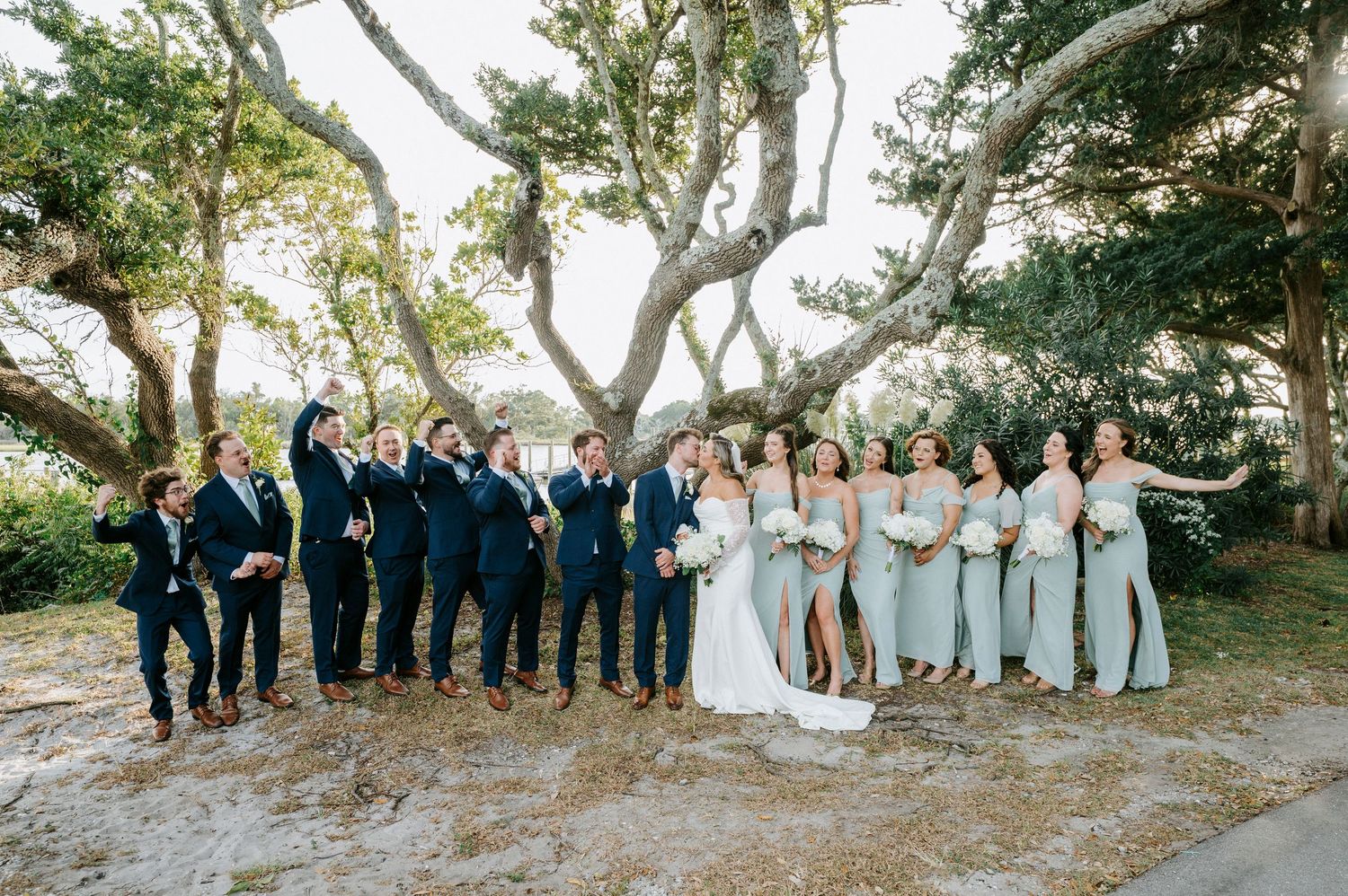 Full wedding party portrait under oak trees with groomsmen and bridesmaids in coordinated attire.