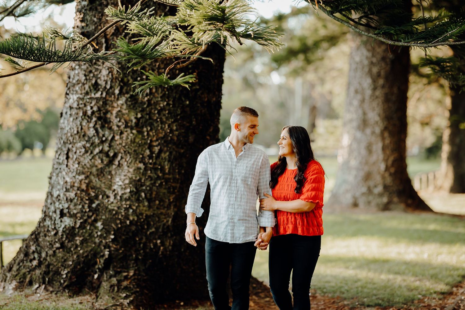 Happy couple holding hands and laughing during an autumn engagement photo session in a wooded park setting.