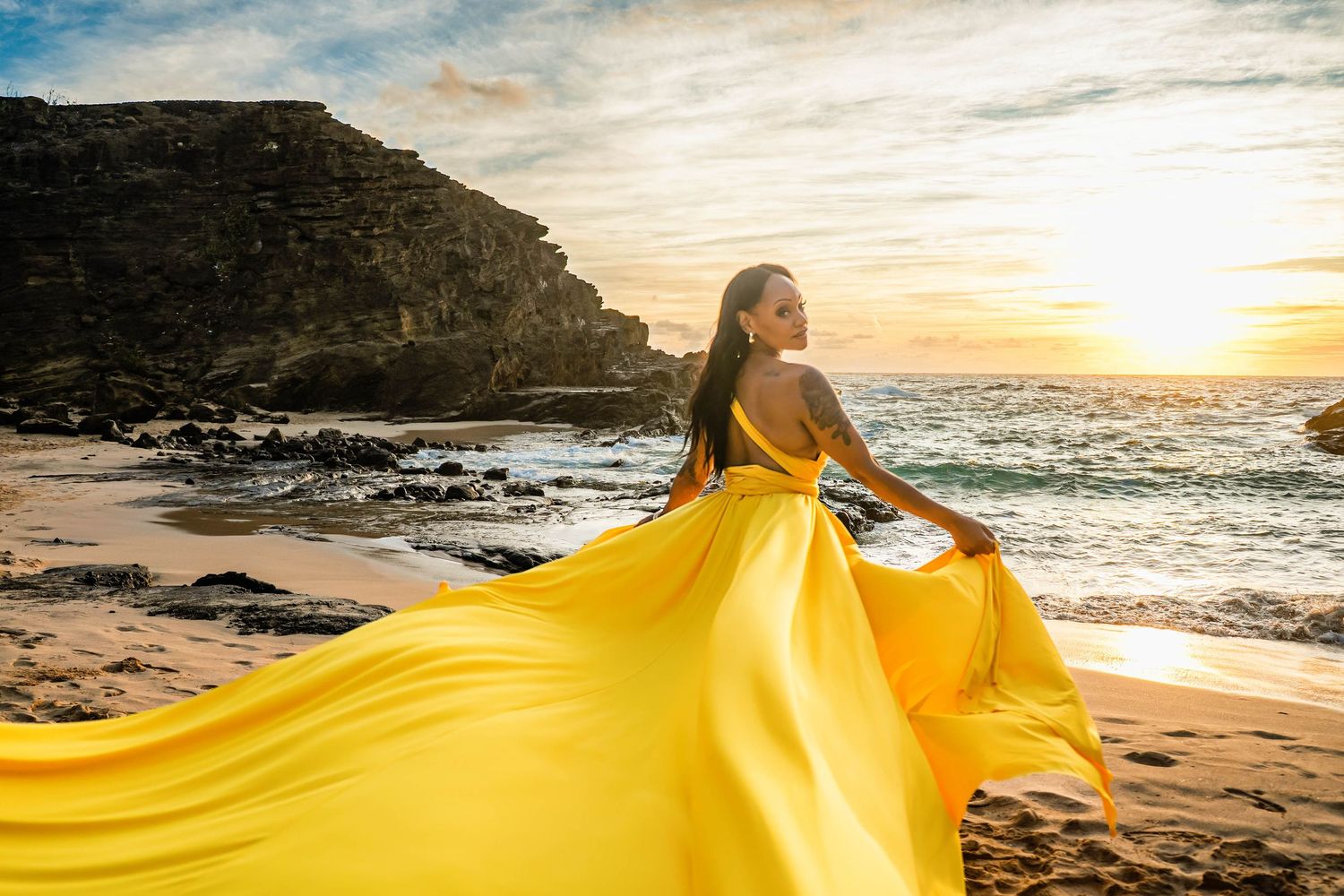 Large flowing yellow dress billows dramatically against a sunset beach shoreline at golden hour.